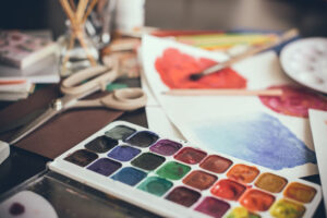 Mess in the the artist's studio, watercolor paints, brushes and sketches, palette and painting tools. Designer's working place, hipster style.